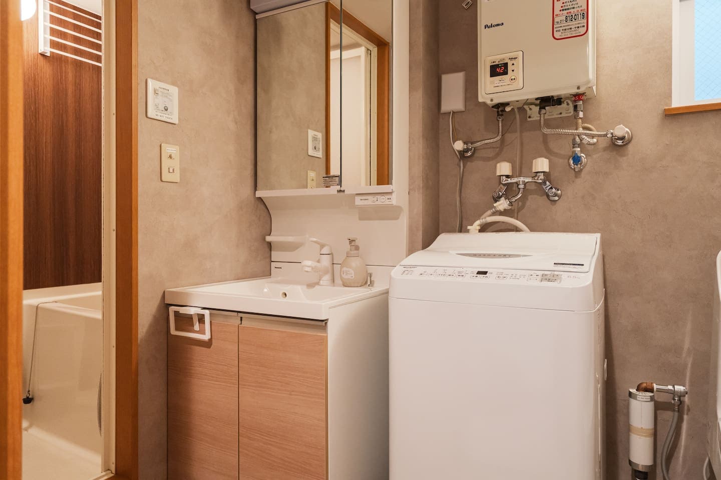 Modern Toilet & Vanity Area.This clean and stylish restroom features a bidet toilet for extra comfort. The bright vanity space includes a wide mirror, ample storage, and a washing machine perfect for extended stays.