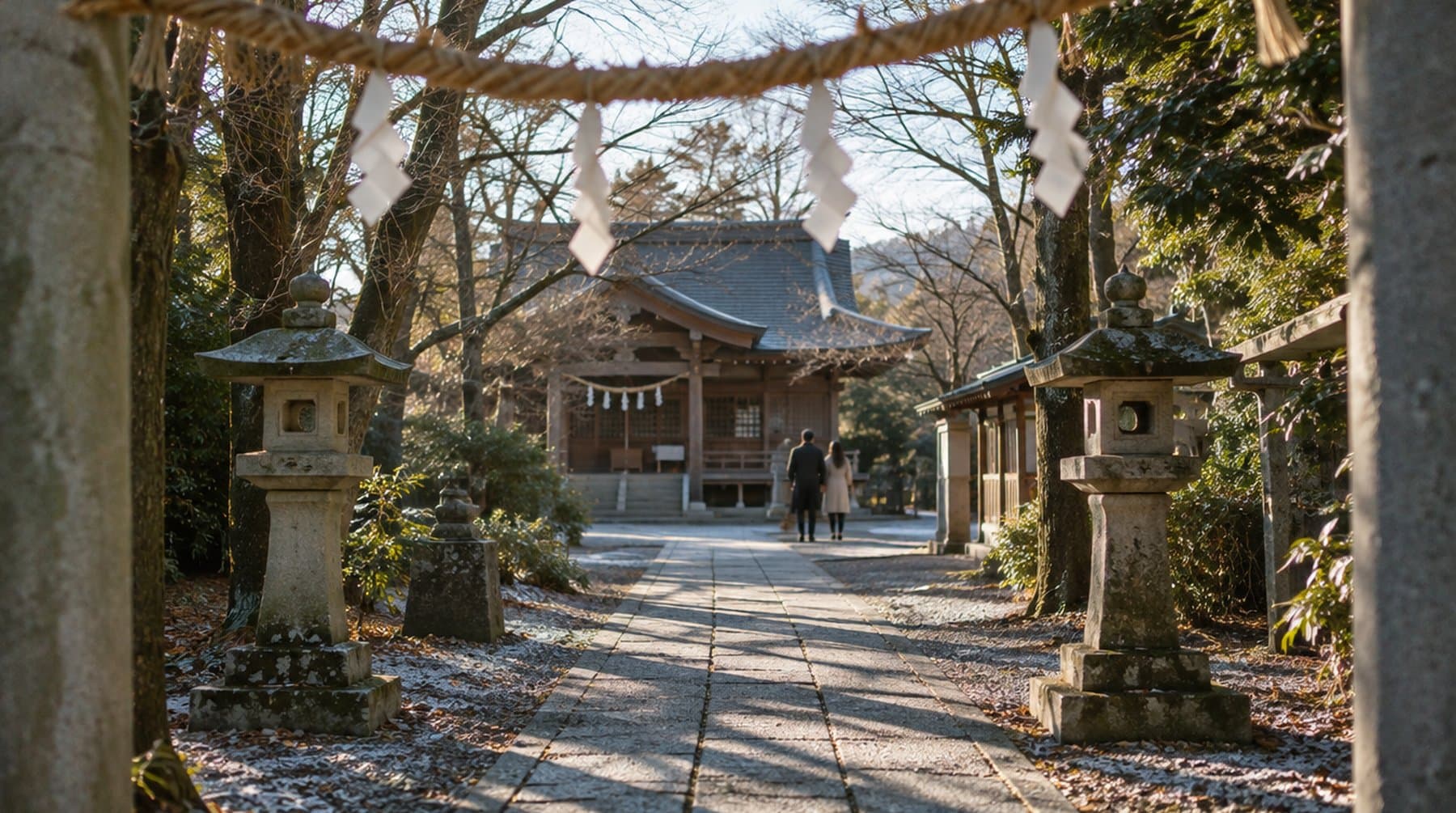 A stone path between lanterns leading to a small wooden shrine on a clear winter morning