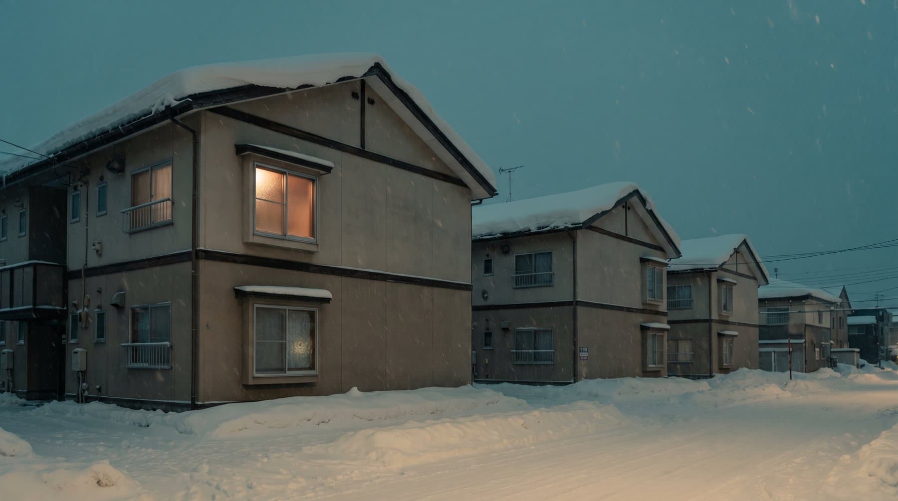 雪の札幌の住宅街、灯りのともる窓