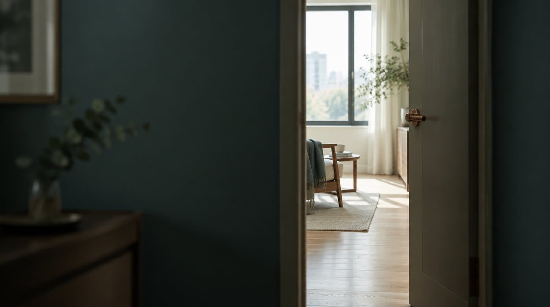 A half-open door seen from a dim hallway, the gap showing only a narrow slice of the bright room beyond